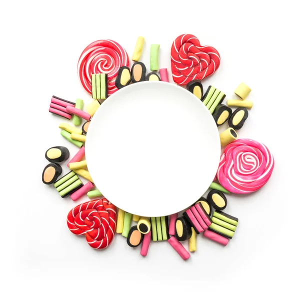 Colorful lollipop and licorice candy around white plate with copy space on white. View from above. Concept banner for design.