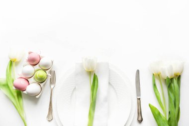 Paskalya akşam yemeği. Tablo ayarı ile Beyaz Lale ve renkli beyaz masaya yumurta. Üstten Görünüm. Metin için yer.