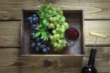 Açık şişe şarap cam, tirbuşon ve olgun üzüm içinde tepsi ahşap arka plan üzerinde. Kopya alanı ve üstten görünüm.