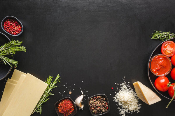 Raw ingredients for lasagna, pasta, vegetables on black. Copy space.