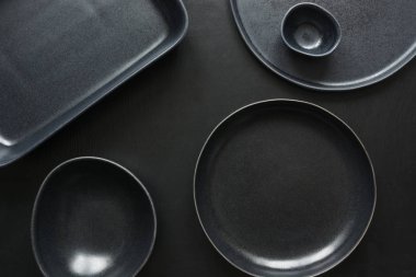 Crockery, clayware, black utensils and different stuff on black tabletop. View from above. clipart