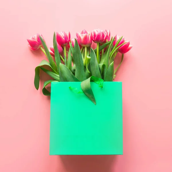 Flores de tulipán rojas frescas en bolsa de papel verde sobre rosa. Primavera . — Foto de Stock