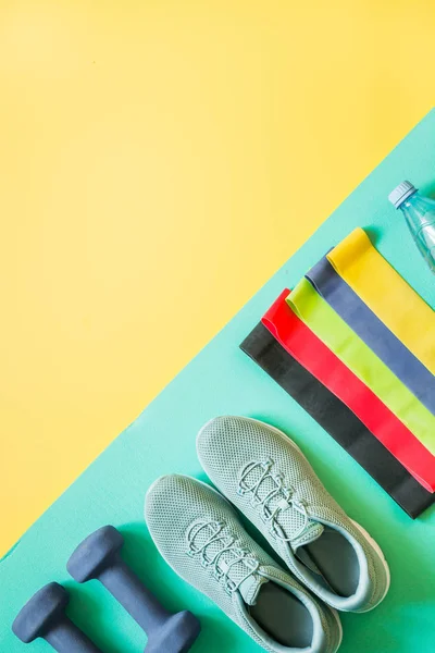 Sport equipment, rubber band, dumbbells, fitness shoes on yellow.