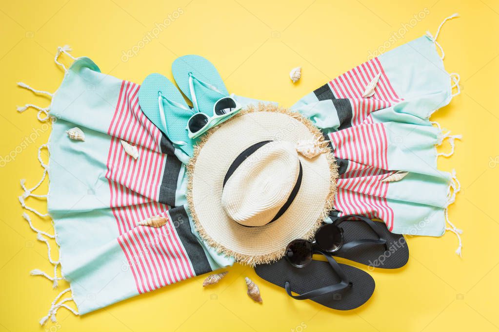 Outfit for beach and tropical vacations, straw beach sunhat,towel, sun glasses on yellow. Summer vacations concept.