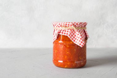 Domates, sarımsak, biber kavanoz ışık arka plan üzerinde sebze sos adjika.