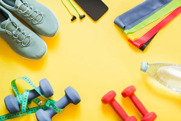 Sport and fitness equipment, dumbbells, fitness shoes, measuring tape on punchy yellow.