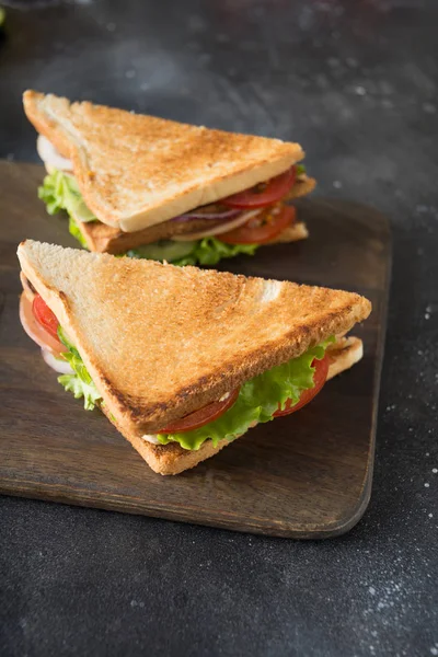 Two sandwiches with bacon,tomato, onion, salad on chopping board and dark. Close up. — Stock Photo, Image