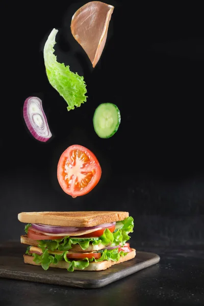 Flying ingredients for sandwich, bacon, tomato, onion, salad on black.