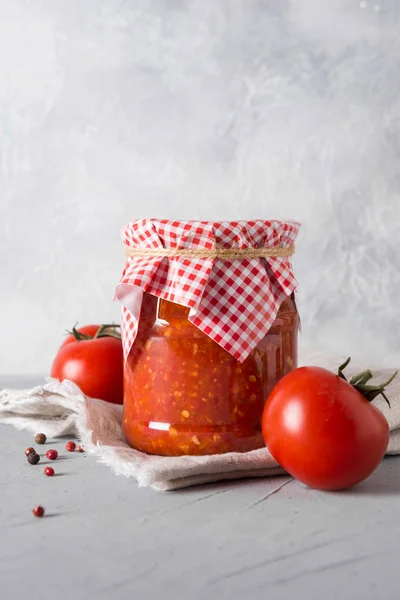 Vegetable sauce adjika with tomatoes, garlic, bell peppers in jar on light background.