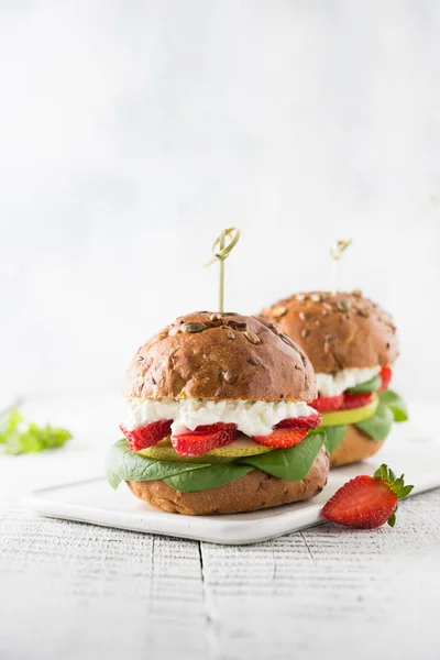 Veggie, vegan burger with strawberry, pear, cottage cheese, and spinach on fresh bun with seeds pumpkin on white board. — Stock Photo, Image