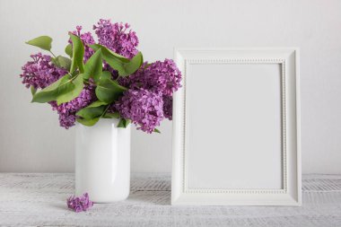 Beyaz fotoğraf çerçevesi ve vazoda mor leylak çiçekleri. Metin için boşluk.