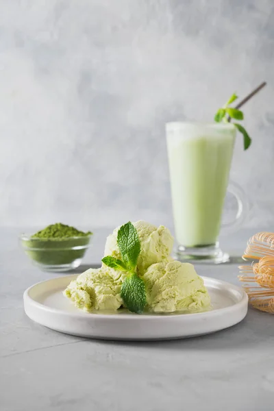 灰色桌上的拿铁玻璃中的绿色火柴冰淇淋和茶. — 图库照片