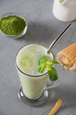 Gri masada buz küpü ve süt ile latte cam yeşil soğuk Matcha çay.