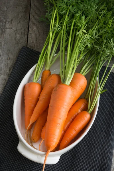 Zanahorias orgánicas frescas con tapas verdes en plato blanco en la mesa. Copiar espacio. Vista superior . — Foto de Stock