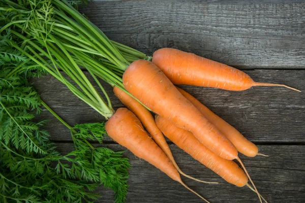 Ahşap masa üzerinde yeşil tops ile taze organik havuç, çekim. Üst görünüm.