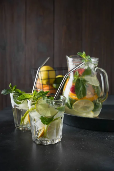 排毒柠檬水与石灰,橙子,柠檬,草莓在玻璃和罐子。夏季健康新鲜饮料。深色木制背景. — 图库照片