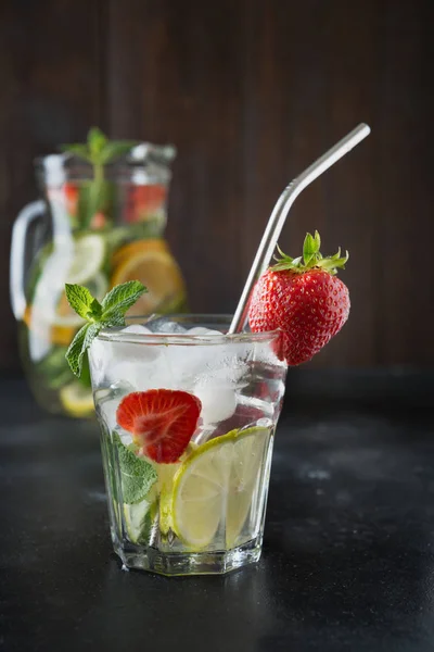 排毒柠檬水与石灰，橙子，柠檬，草莓在玻璃和壶。夏季健康新鲜饮料。深色木制背景. — 图库照片