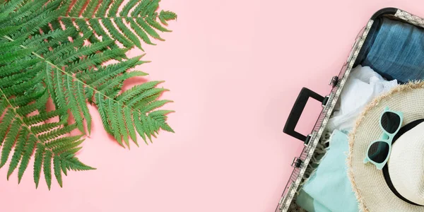 Leaf of fern, tropical detox water and open suitcase with clothes on pastel pink. Top view with copy space. Summer concept travel. — Stock Photo, Image