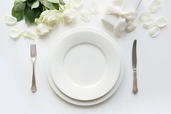 Білий стіл з букетом троянди, подарунок, посуд, посуд на святковому білому столі. Вид зверху. Романтична та весільна річниця . — стокове фото