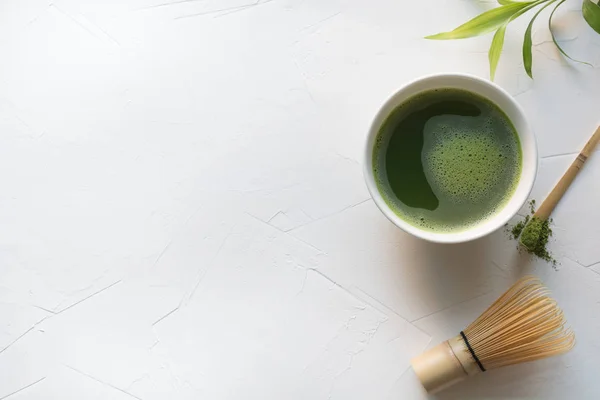 Ünnepség zöld Matcha tea és bambusz Habverő a fehér beton asztalra. Felülnézet. — Stock Fotó