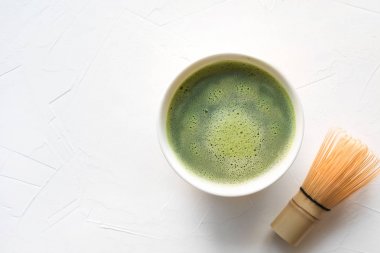 Yeşil matcha çay ve beyaz beton masa üzerinde bambu çırpıcı. Üstte görüntü.