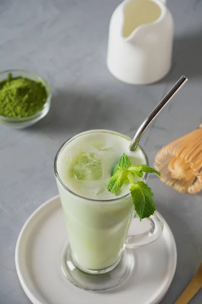 在拿铁杯中加入绿色冷火柴茶,在灰色桌子上配冰块和牛奶。特写从上面查看. — 图库照片