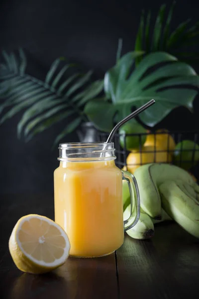 Friss nyári gyümölcsök gyümölcslé banánnal, citrommal, sötét trópusi háttérrel. — Stock Fotó