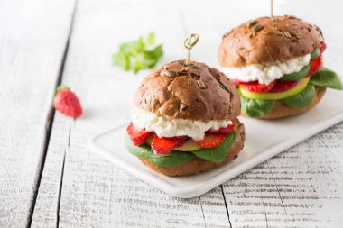 Çilek, armut, süzme peynir ve beyaz ahşap tahta üzerinde tohum kabak ile taze topuz üzerinde ıspanak vegan burger. Metin için alan.