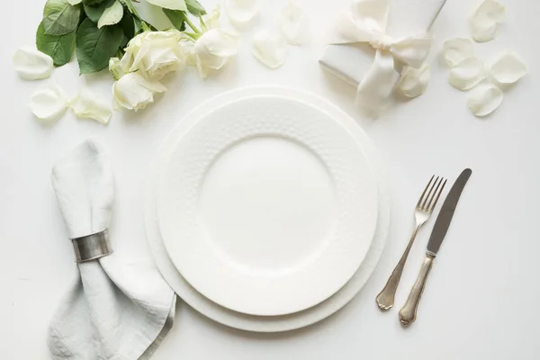 Білий стіл з букетною трояндою, подарунком, посудом, посудом на білому столі. Вид зверху . — стокове фото