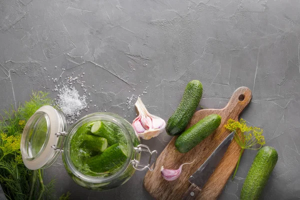 Okurka a fermentační okurky ve skleněné nádobě s dillem a česnekem na šedém stole. Pohled shora. — Stock fotografie