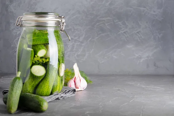 Okurka a fermentační okurky ve skleněné nádobě s dillem a česnekem na šedé. Místo pro text. — Stock fotografie