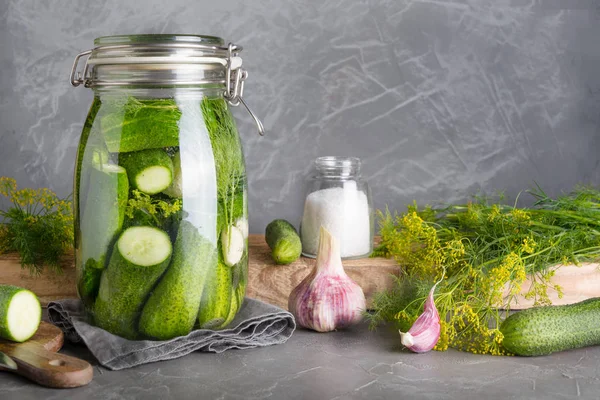 Okurka a fermentační okurky ve skleněné nádobě s dillem a česnekem na šedé. Místo pro text. — Stock fotografie