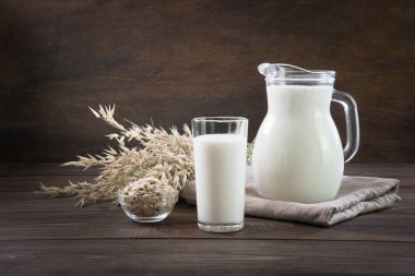 Fresh oat milk in glass and pitcher on dark wooden table. Rustic style. clipart
