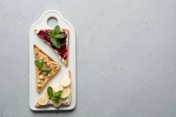 Tres sándwiches sin azúcar para el desayuno, pasta de nueces, plátanos, mermelada de bayas. Espacio para texto . — Foto de Stock