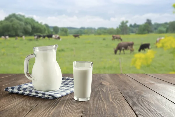 어두운 나무 테이블에 유리에 신선한 우유와 초원에 소와 흐린 풍경. — 스톡 사진
