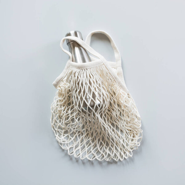 Empty shopping mesh bag with metal bottle on grey. Zero waste co