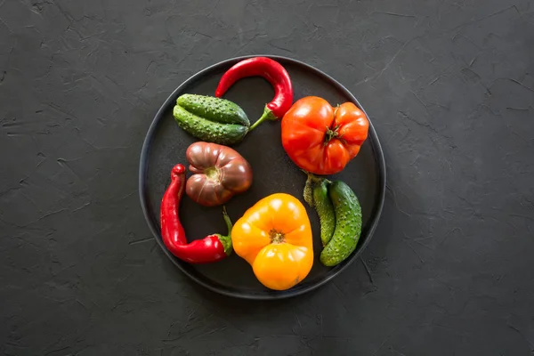 Feo tomate colorido orgánico, pimienta, pepino en plato en hormigón negro. Concepto verduras ecológicas . —  Fotos de Stock