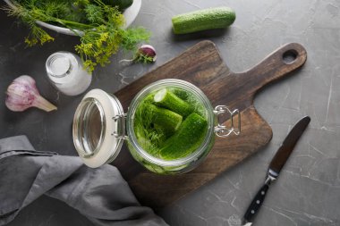 Koyu gri beton masada dereotu ve sarımsak ile cam kavanozda turşu ve fermantasyon salatalık.