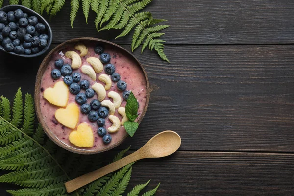 Desayuno saludable de plátano y batido de arándanos decorado con frutas en un bol de coco. — Foto de Stock