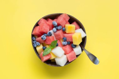 Sarı arka plan üzerinde hindistan cevizi kase karpuz, kavun ve mango meyve salatası.