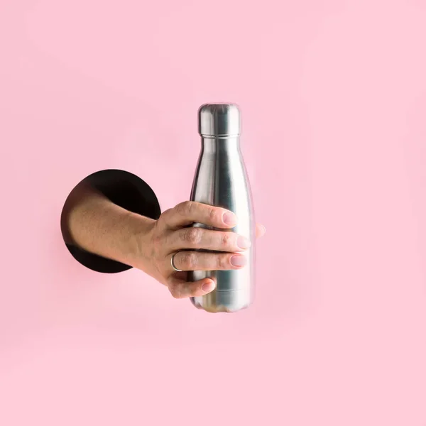 ピンクの穴を通して女性の手で金属再利用可能なボトル. — ストック写真