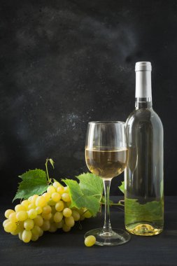 Şarap kadehi ile beyaz şarap şişesi, siyah ahşap masa üzerinde olgun üzüm.