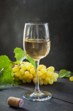 Şarap kadehi ile beyaz şarap şişesi, siyah ahşap masa üzerinde olgun üzüm.