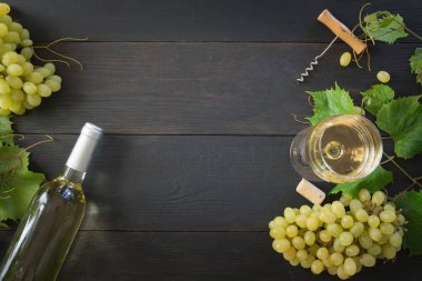 Şarap kadehi ile beyaz şarap şişesi, siyah ahşap masa üzerinde olgun üzüm.