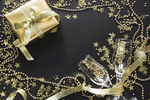 Πολυτελές χρυσό κουτί δώρου με δύο γυάλινες σαμπάνιας σε λαμπερό μαύρο φόντο. Χριστουγεννιάτικο πάρτι. "Επίπεδη". Θέα από πάνω. Χριστούγεννα. — Φωτογραφία Αρχείου