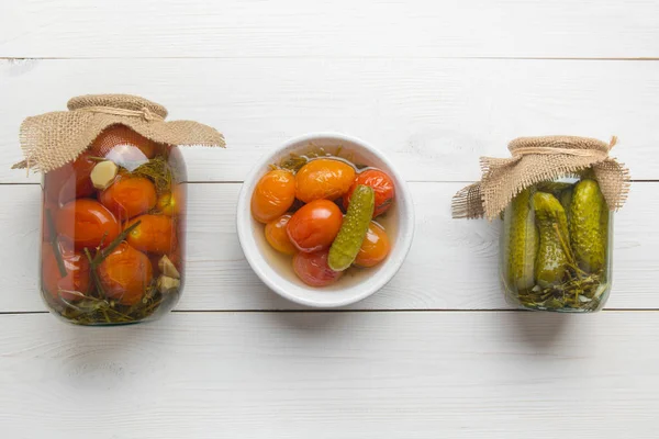 Canned vegetables cucumber and tomato in glass jars on wooden board. View from above. Homemade harvest fall preparations. Homework and traditions.