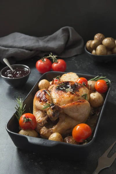 Roasted chicken with potato on black table.