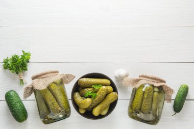 Beyaz ahşap tahta üzerinde cam kavanozlarda konserve sebze salatalık. Yukarıdan görüntüleyin. Metin için alan.