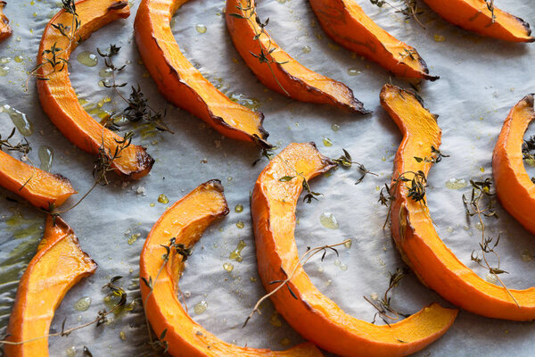 Hot roasted slices pumpkin with thyme, olive oil and salt on baking paper. Tasty vegan food.