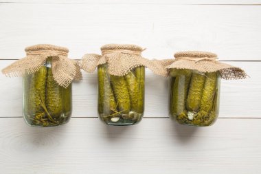 Beyaz ahşap tahta üzerinde cam kavanozlarda konserve sebze salatalık. Yukarıdan görüntüleyin. Metin için alan.